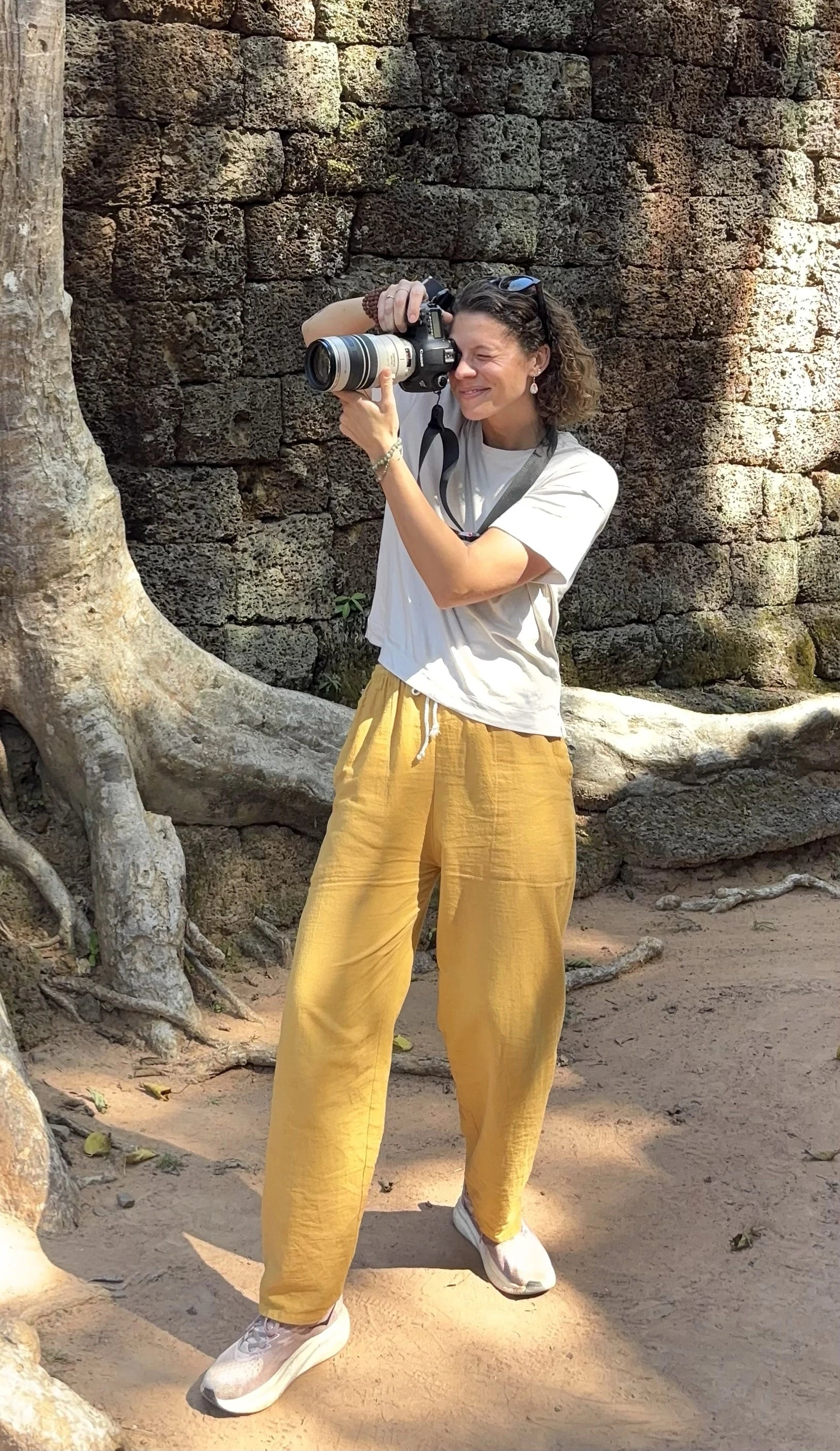 Bronwyn Huddleson is taking a photo with a camera in front of stone walls and large tree roots